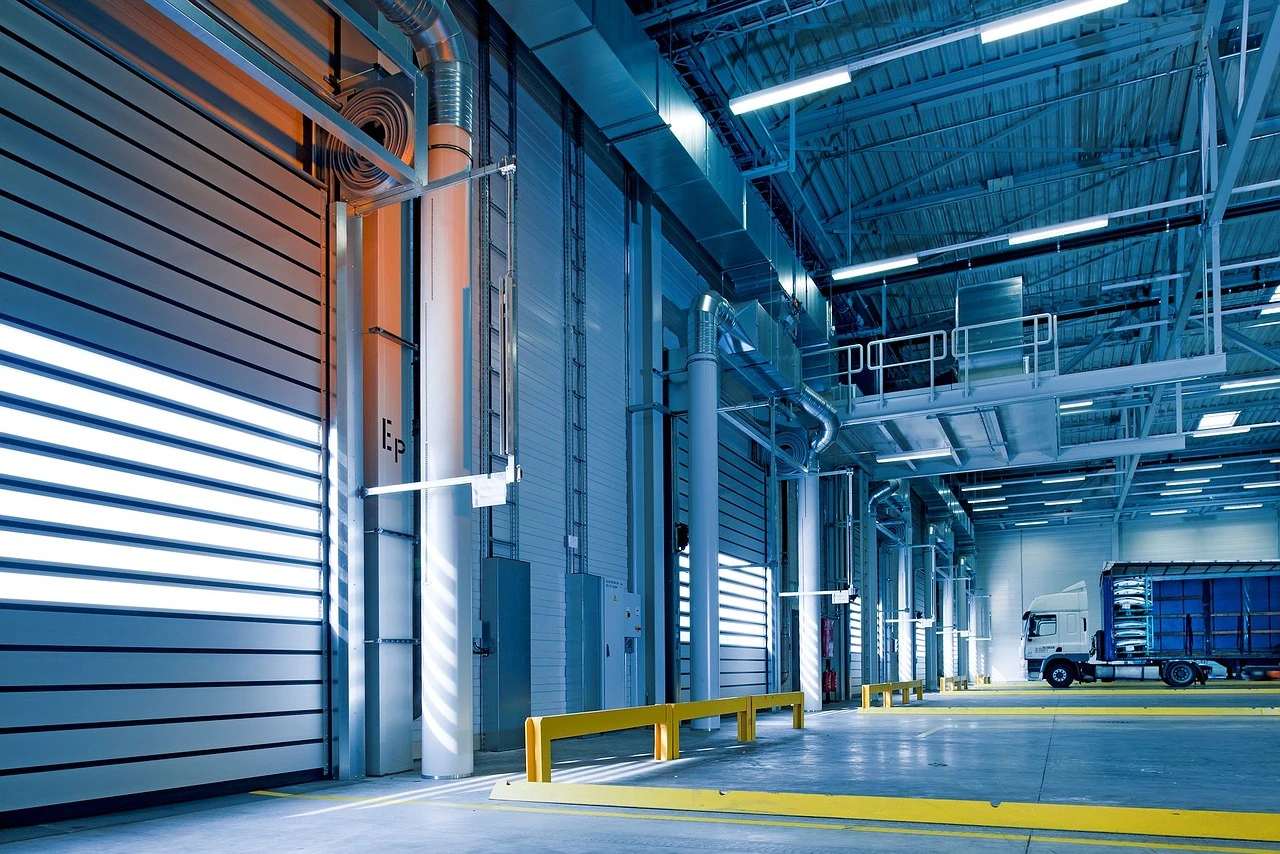 Interieur van een magazijnhal met ge&iuml;nstalleerde industri&euml;le rolpoorten, een verlichte werkruimte met oprit en laadzone.